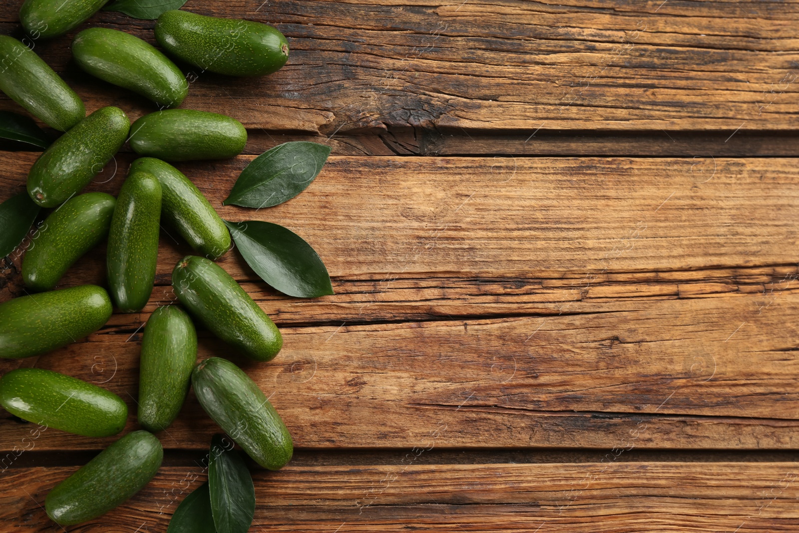 Photo of Fresh avocados with green leaves on wooden table, flat lay. Space for text