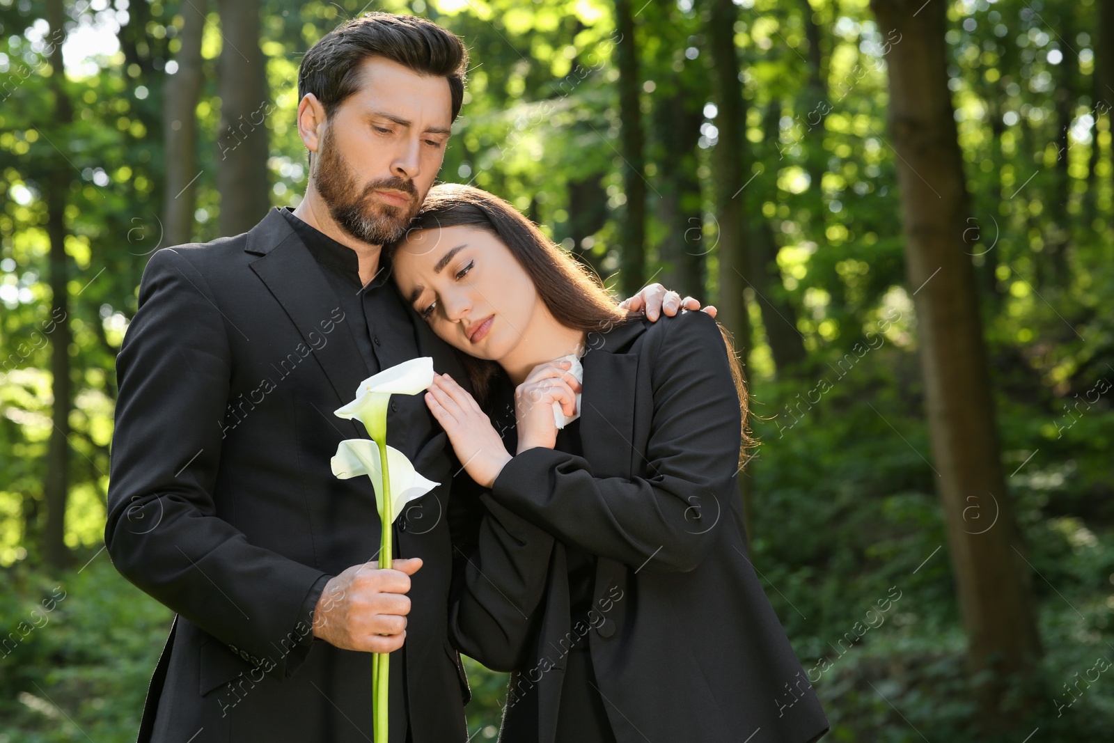 Photo of Sad couple with white calla lily flower mourning outdoors, space for text. Funeral ceremony