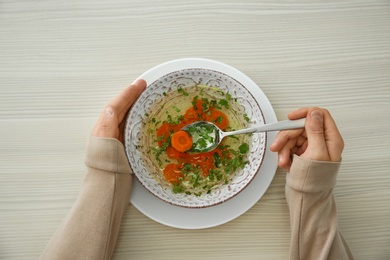 Photo of Man with bowl of soup at wooden table, top view. Flu treatment