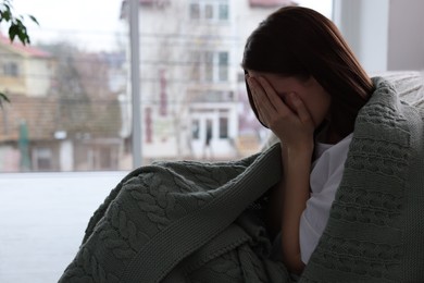 Photo of Sad young woman wrapped in warm plaid crying at home, space for text. Loneliness concept