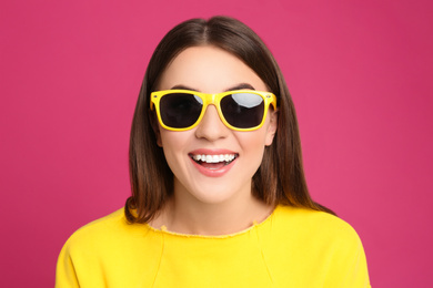 Young woman with sunglasses on pink background