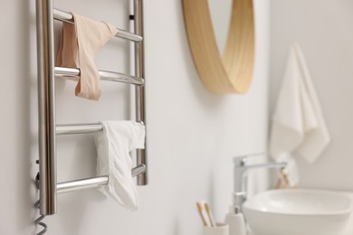 Photo of Heated towel rail with underwear on white wall in bathroom, closeup