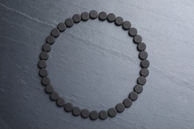 Photo of Frame of activated charcoal pills on black table, flat lay with space for text. Potent sorbent