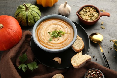 Photo of Delicious pumpkin soup in bowl served on grey textured table
