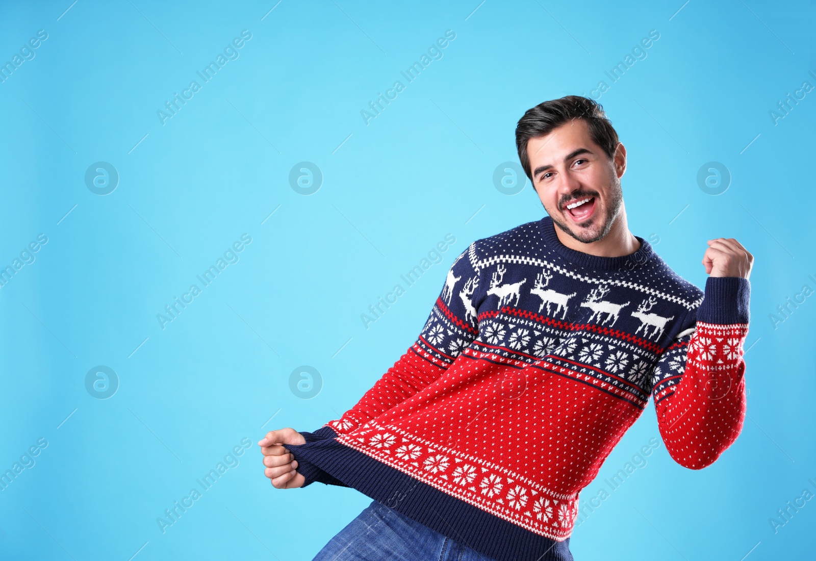 Photo of Portrait of happy young man in Christmas sweater on light blue background