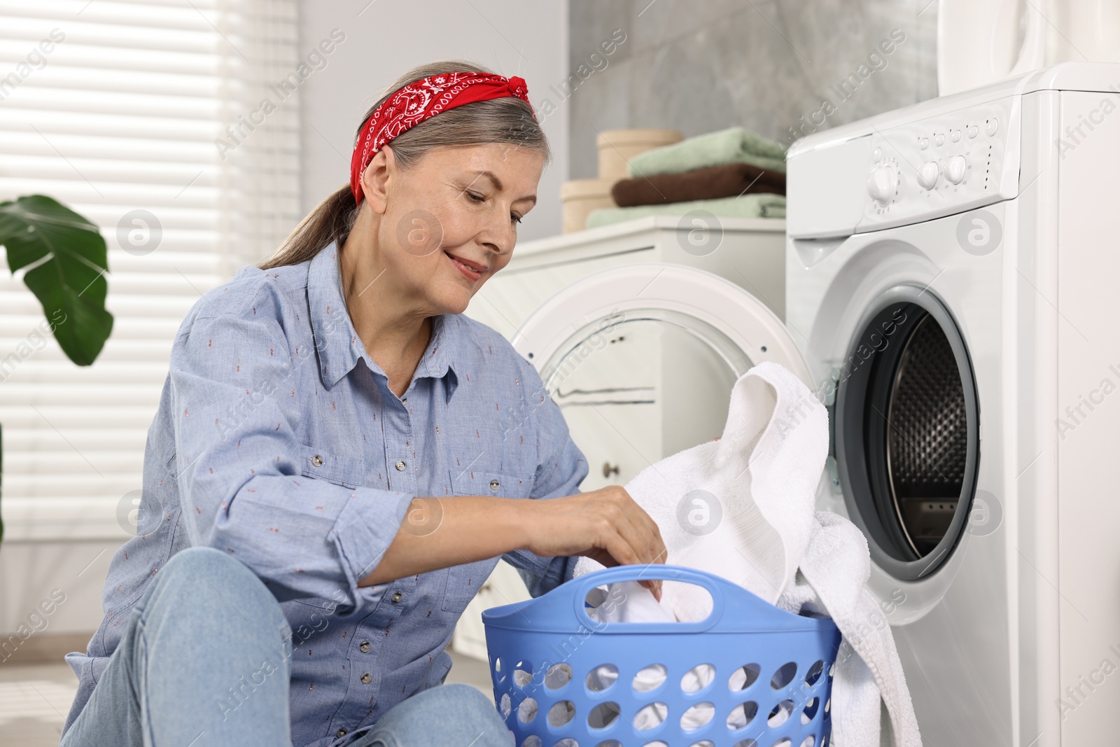 Photo of Happy housewife with laundry basket near washing machine at home