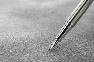 Photo of Stylish silver fountain pen on grey textured table, closeup. Space for text