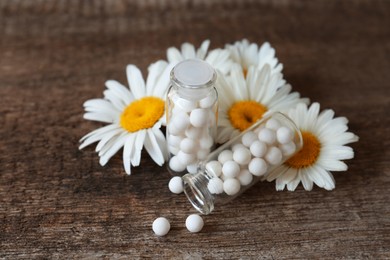 Photo of Bottles with homeopathic remedy and flowers on wooden table