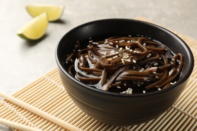 Photo of Tasty buckwheat noodles (soba) with sauce in bowl and chopsticks on table, closeup