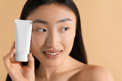 Photo of Beautiful young woman holding sun protection cream on beige background, space for text
