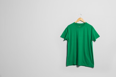 Photo of Hanger with green t-shirt on light wall. Mockup for design