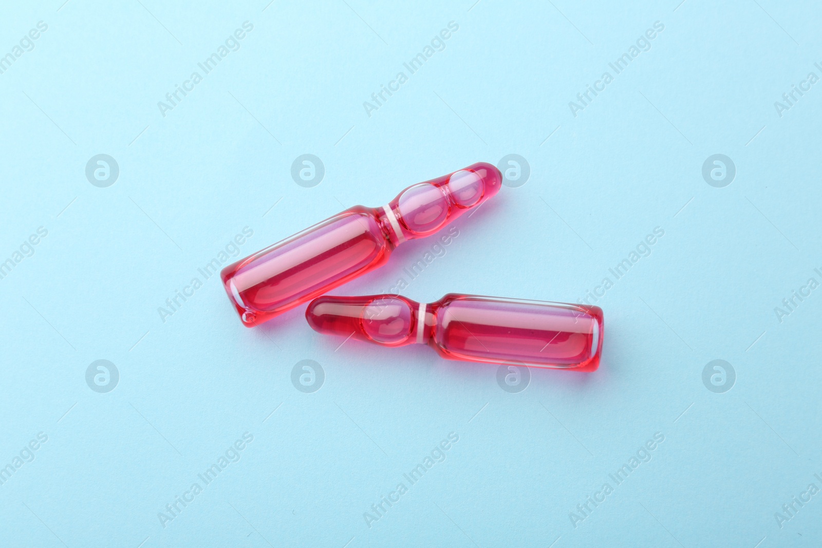 Photo of Glass ampoules with liquid on light blue background, top view