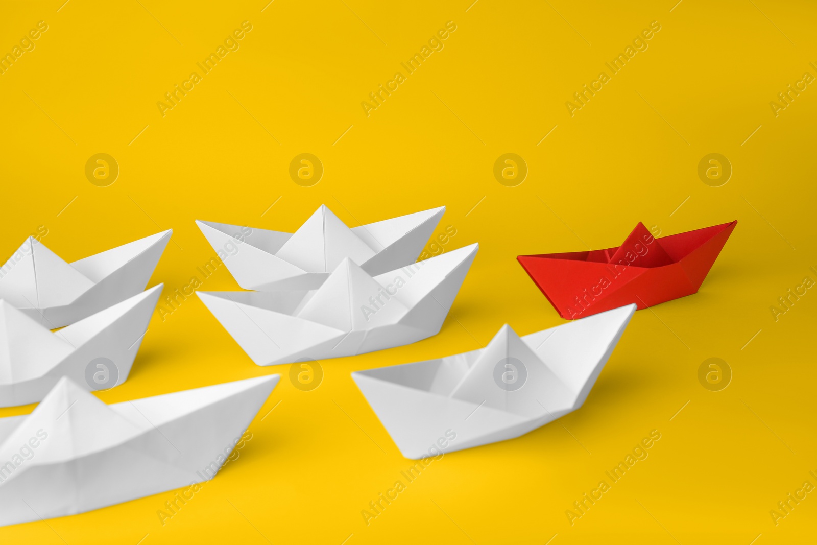 Photo of Group of paper boats following red one on yellow background. Leadership concept