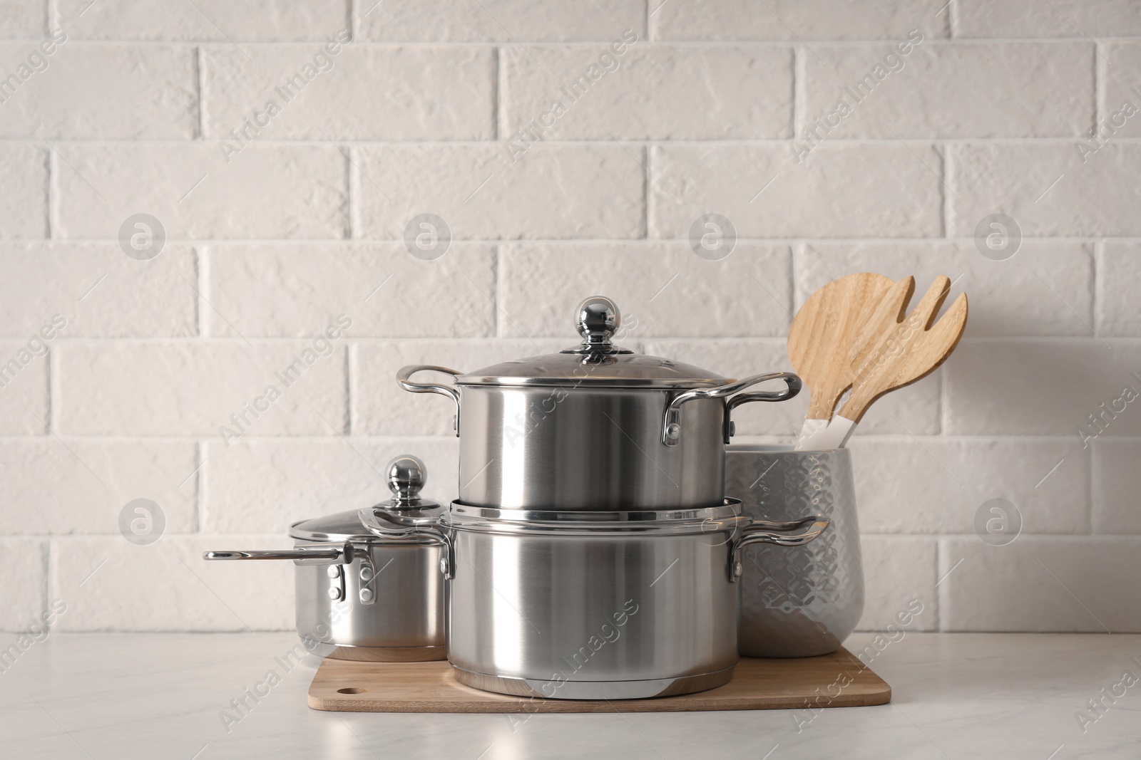 Photo of Set of stainless steel cookware and kitchen utensils on table near white brick wall