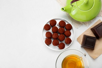 Photo of Delicious chocolate candies powdered with cocoa and tea on white table, flat lay. Space for text