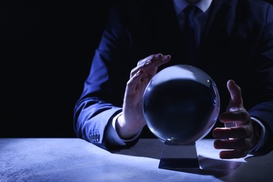 Photo of Businessman using crystal ball to predict future at table in darkness, closeup. Space for text