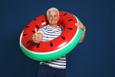 Photo of Funny mature man with bright inflatable ring on dark blue background