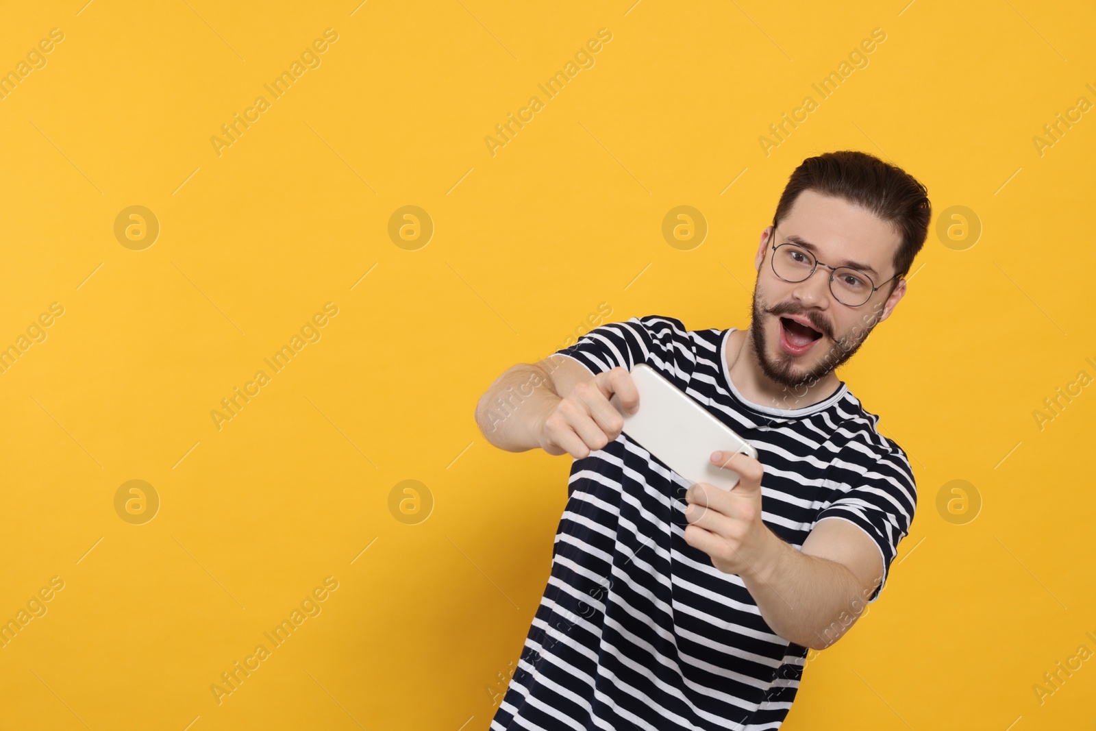 Photo of Emotional man playing game on phone against orange background. Space for text