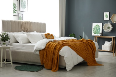 Comfortable bed with knitted orange plaid in stylish room interior