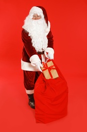 Photo of Authentic Santa Claus with sack and gift on red background