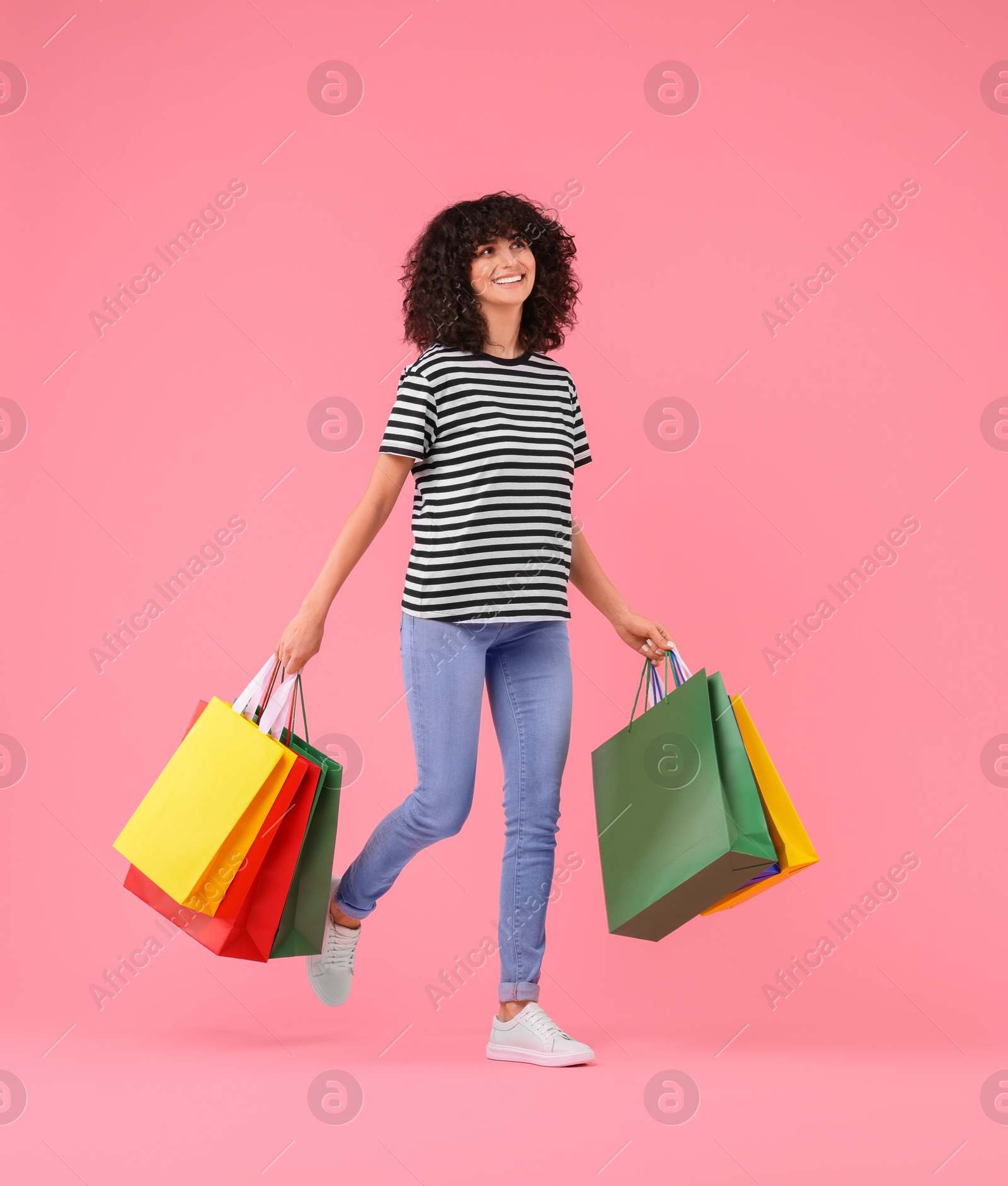 Photo of Happy young woman with shopping bags on pink background