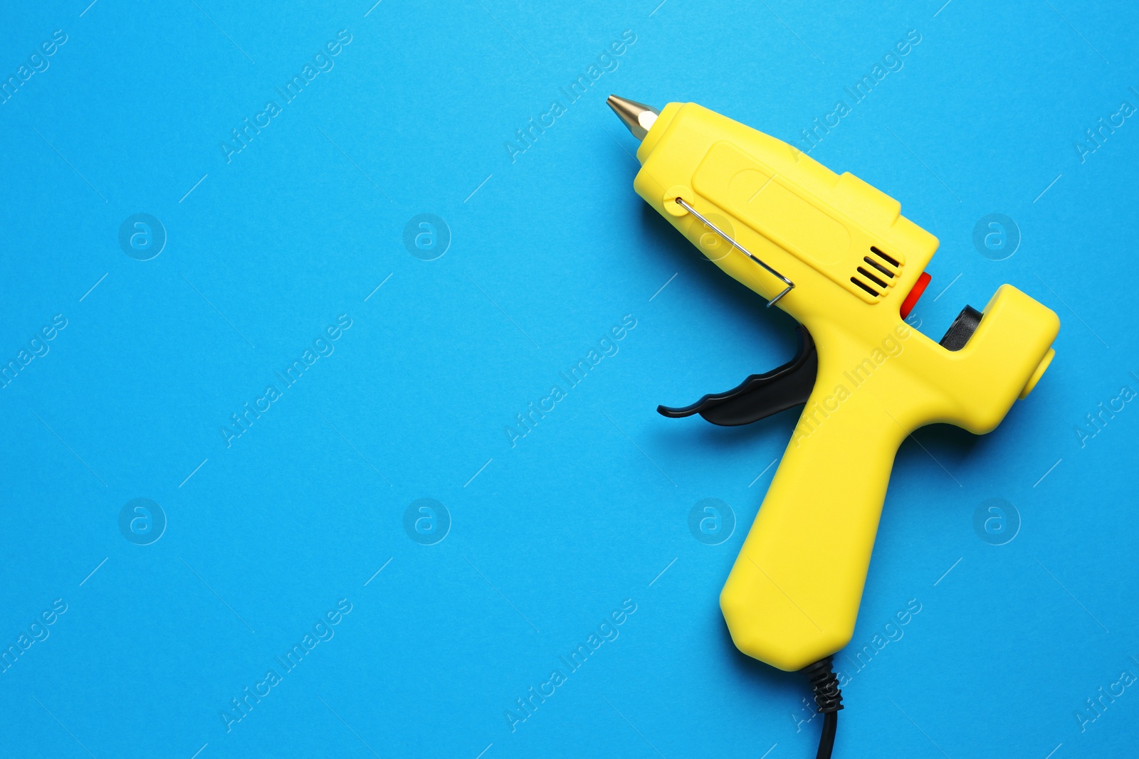 Photo of Empty yellow glue gun on light blue background, top view. Space for text
