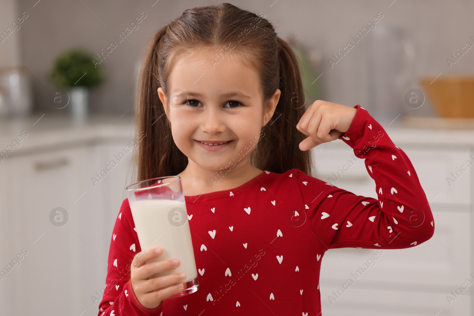 Photo of Cute girl with glass of fresh milk showing her strength in kitchen