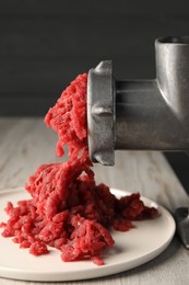 Mincing beef with metal meat grinder on light wooden table, closeup