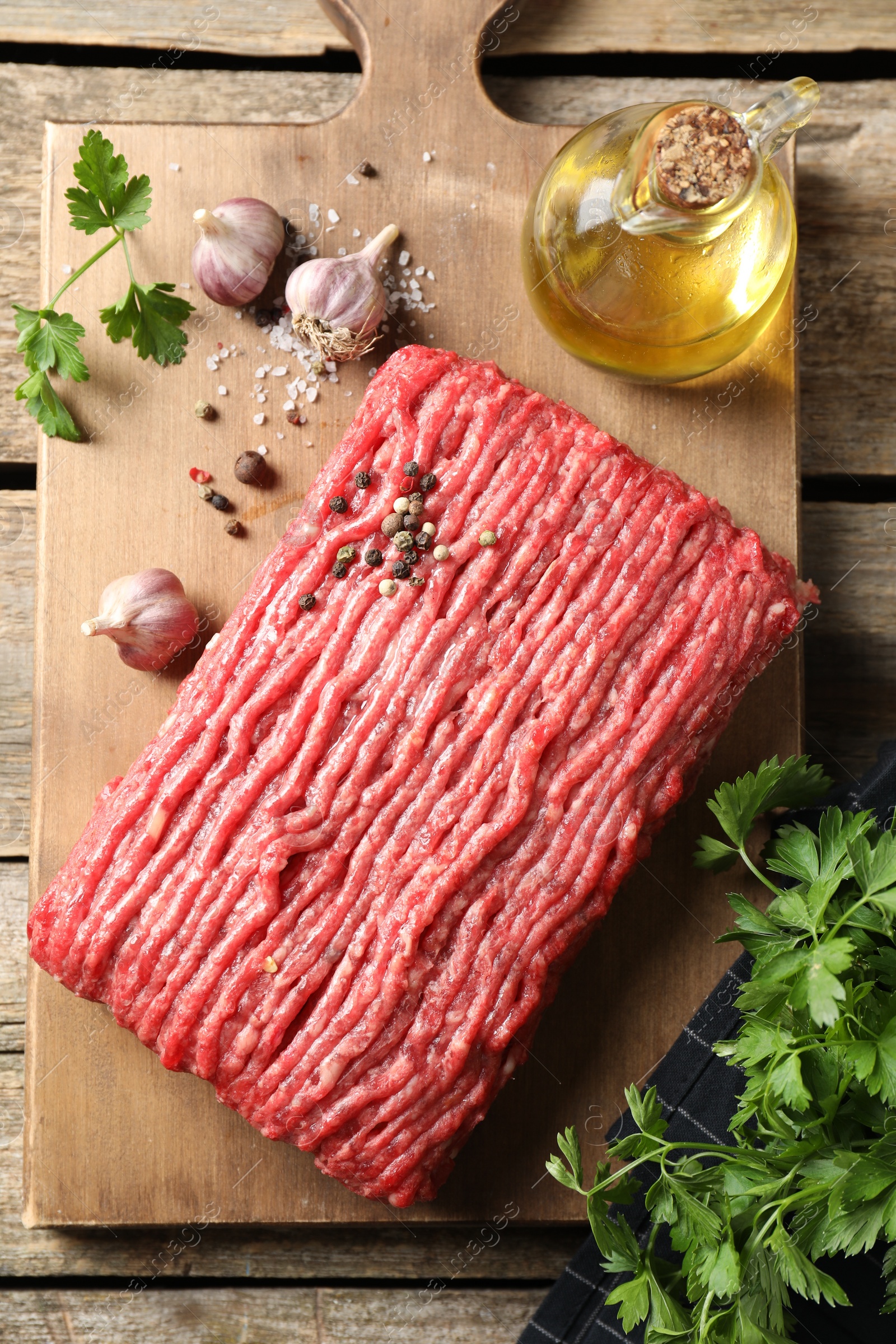 Photo of Raw ground meat, spices, parsley and oil on wooden table, top view