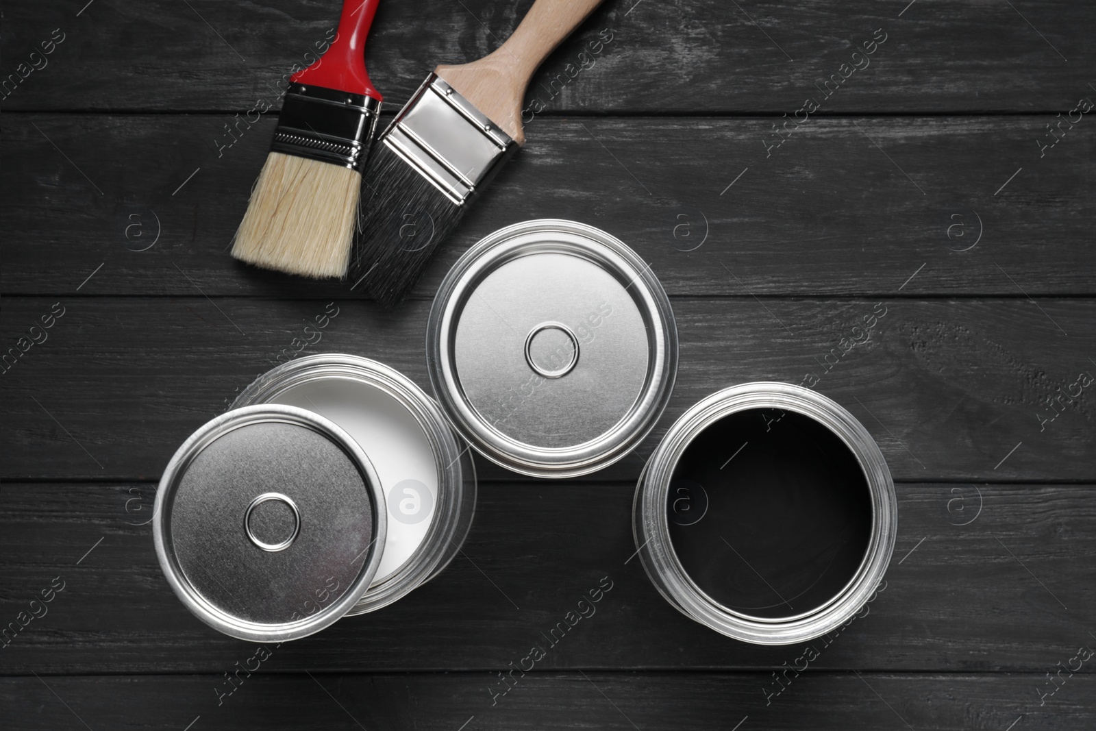 Photo of Cans of white and black paints with brushes on wooden table, flat lay