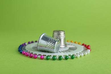 Photo of Sewing thimbles and pins on green background, closeup
