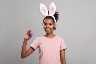 Happy African American woman in bunny ears headband with Easter egg on gray background