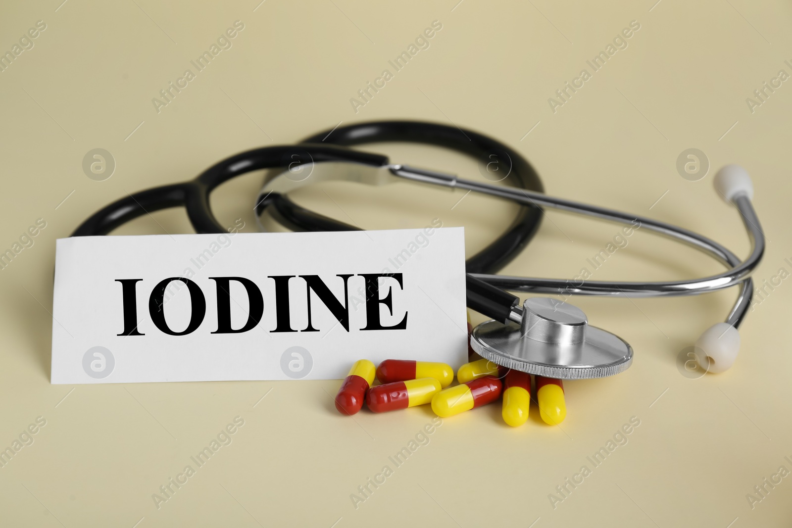 Photo of Card with word Iodine, stethoscope and pills on beige background