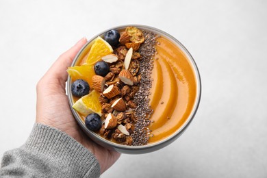 Photo of Woman holding bowl of delicious fruit smoothie with fresh orange slices, blueberries and granola on white background, closeup
