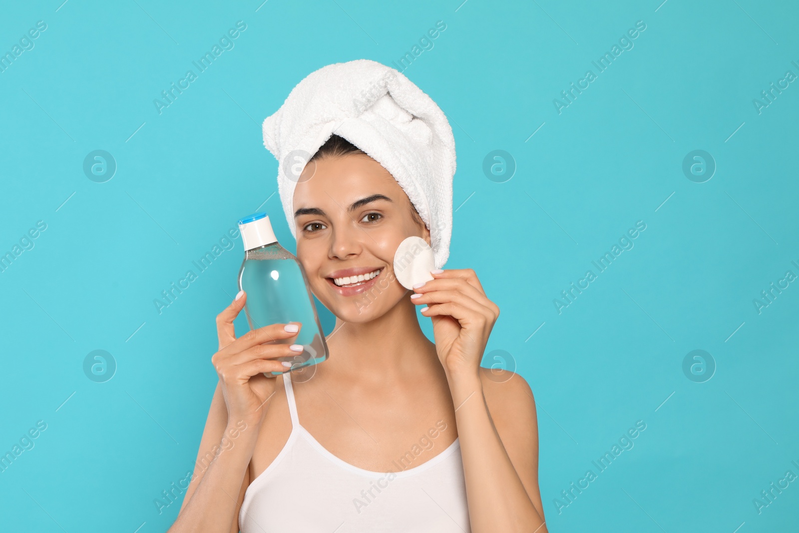 Photo of Young woman using cotton pad with micellar water on light blue background