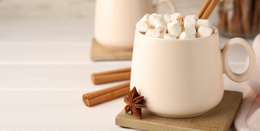 Photo of Cup of hot drink with marshmallows and aromatic cinnamon on white table. Space for text