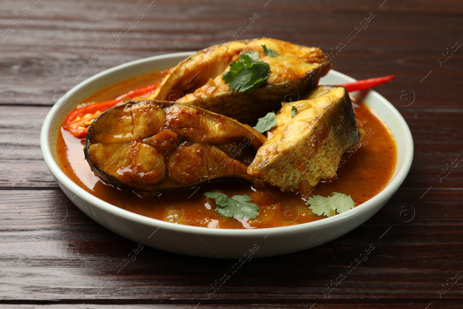 Photo of Tasty fish curry on wooden table, closeup. Indian cuisine