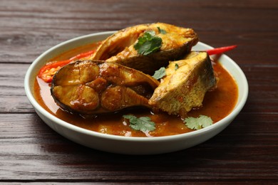 Photo of Tasty fish curry on wooden table, closeup. Indian cuisine