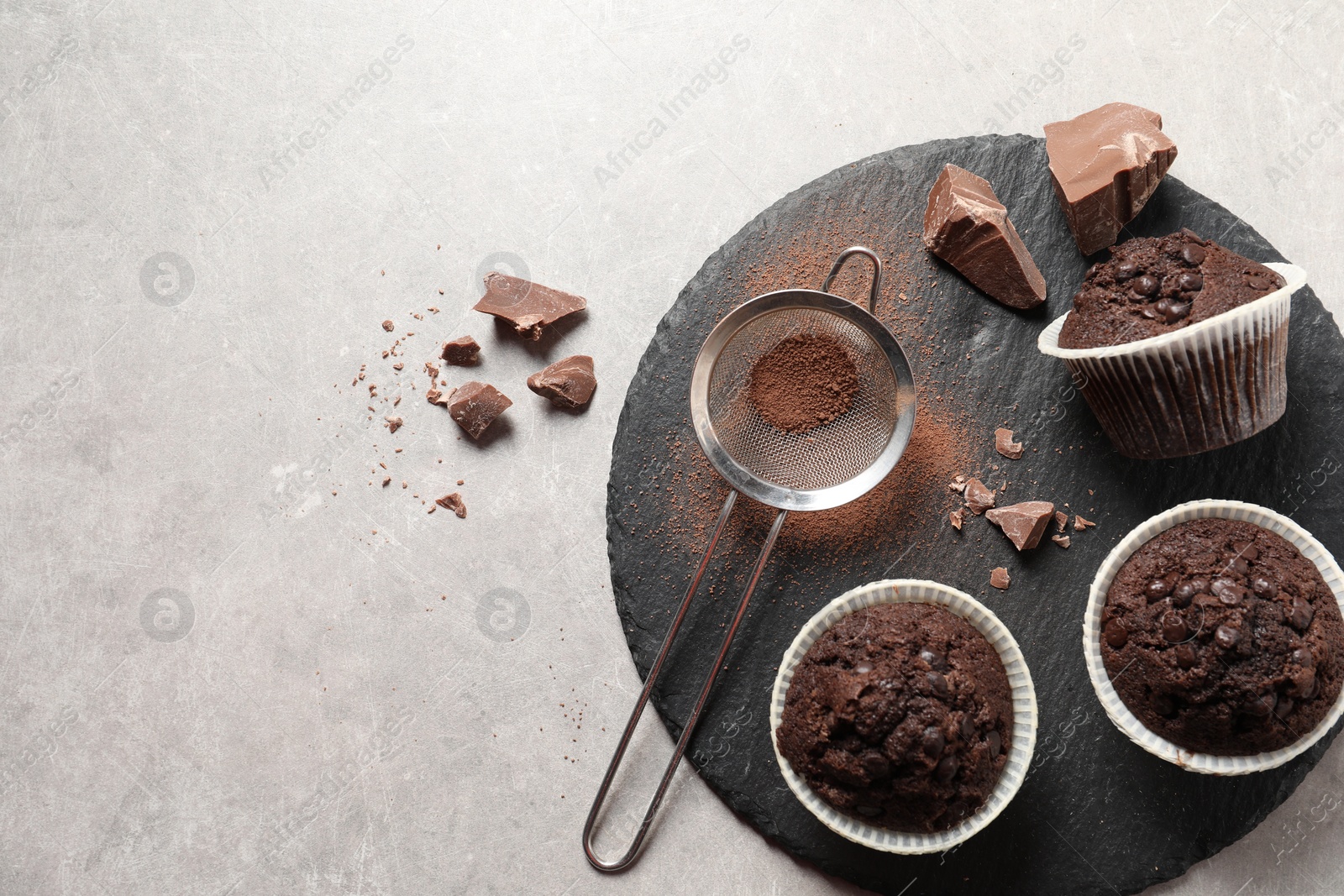 Photo of Delicious chocolate muffins and sieve with cocoa powder on light table, top view. Space for text