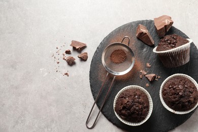 Photo of Delicious chocolate muffins and sieve with cocoa powder on light table, top view. Space for text