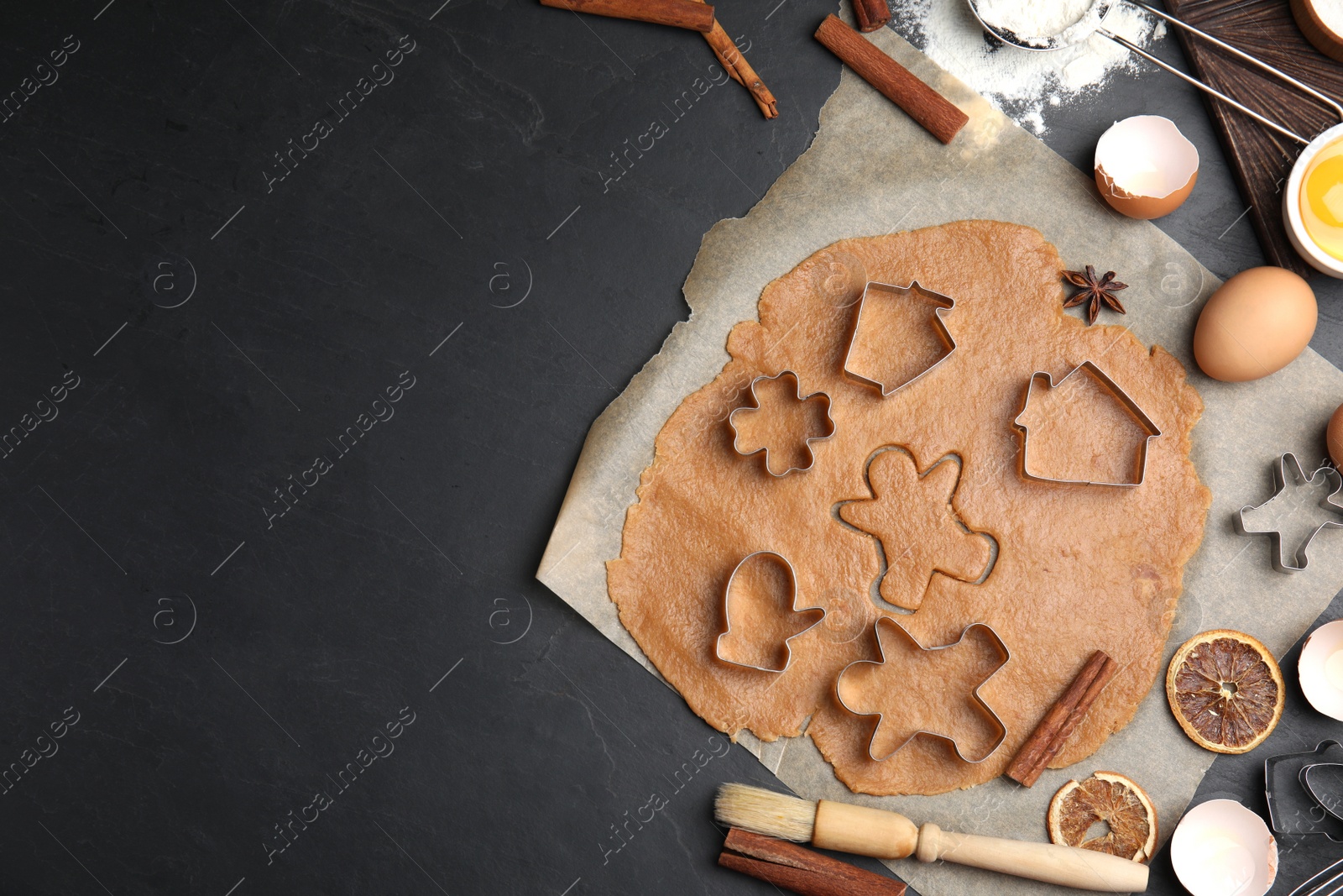 Photo of Dough, different cutters and ingredients for Christmas cookies on black table, flat lay. Space for text