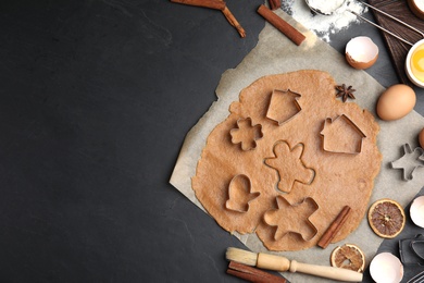 Dough, different cutters and ingredients for Christmas cookies on black table, flat lay. Space for text