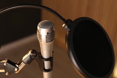 Photo of Stand with microphone and pop filter on blurred background, closeup. Sound recording and reinforcement
