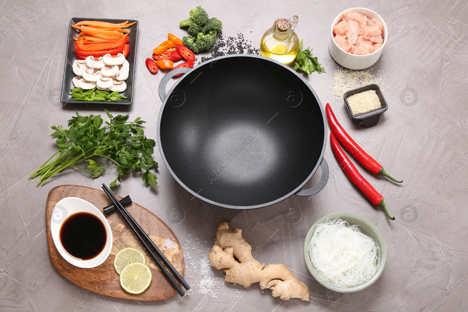 Photo of Wok, chopsticks and different products on grey textured table, above view