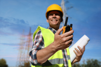 Professional electrician near high voltage tower, focus on hand with portable radio station