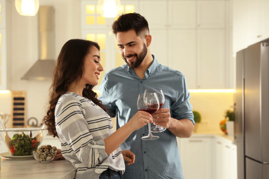 Photo of Lovely young couple drinking wine while cooking together at kitchen