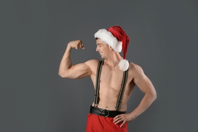 Photo of Young muscular man in Santa hat on gray background