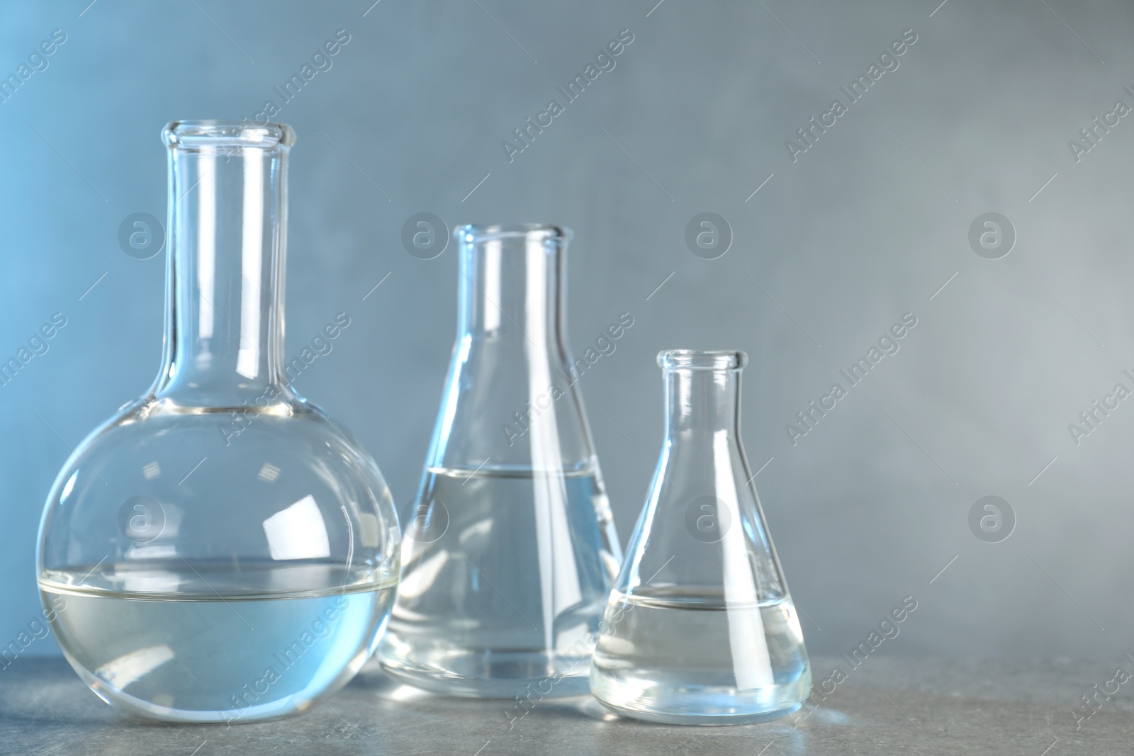 Photo of Laboratory glassware with liquid samples for analysis on grey table against toned blue background