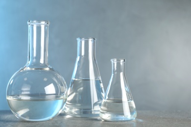 Laboratory glassware with liquid samples for analysis on grey table against toned blue background