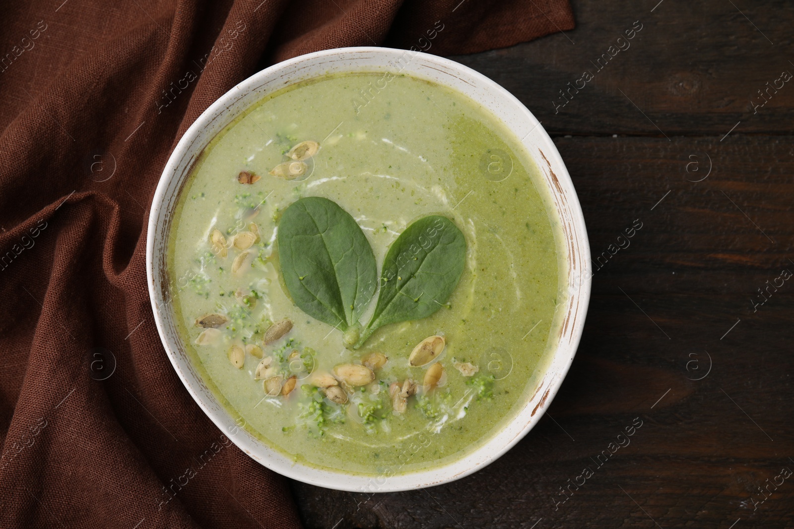 Photo of Delicious broccoli cream soup with basil and pumpkin seeds on wooden table, top view